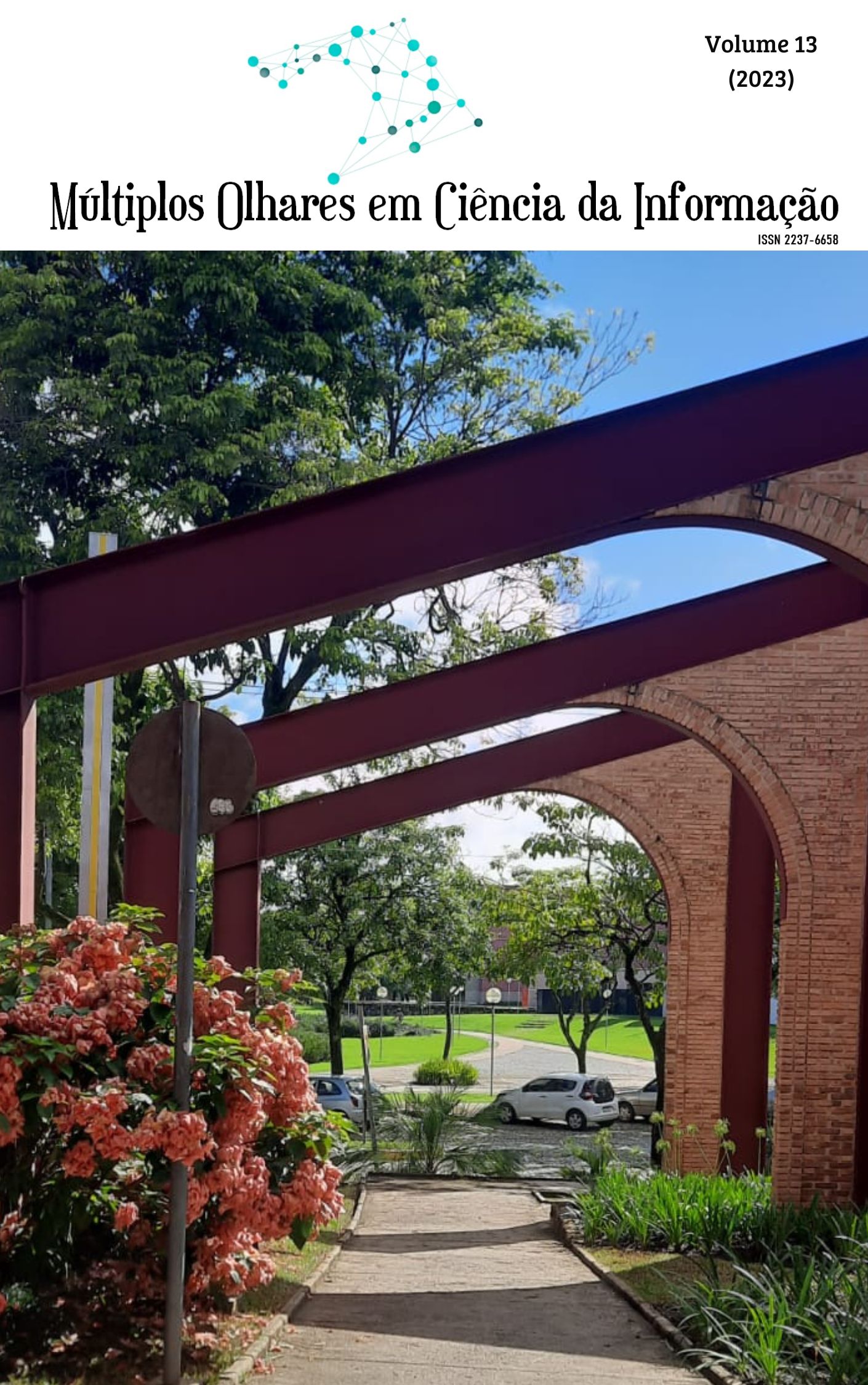 Imagem da praça de serviços da UFMG. Árvore verde à esquerda, flores rosas na frente da árvore, uma estrada no centro e um gramado verde à direita.